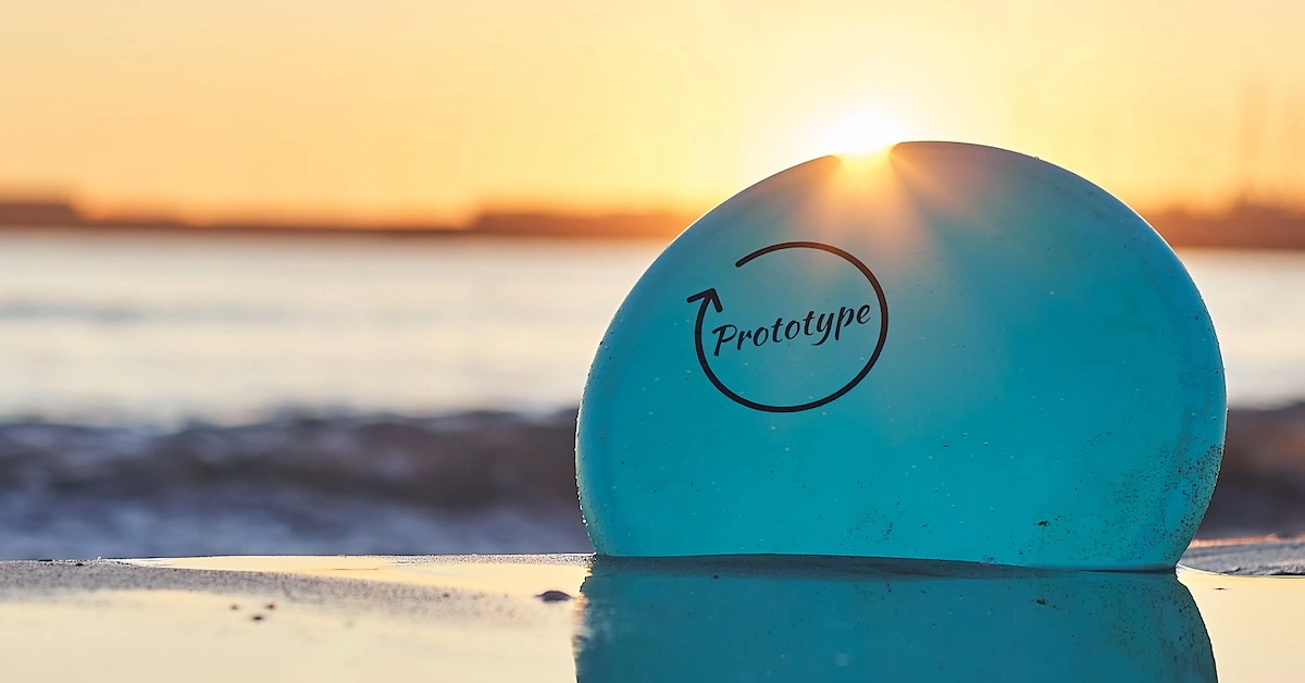 A disc partially buried in beach sand in front of the ocean and sunset