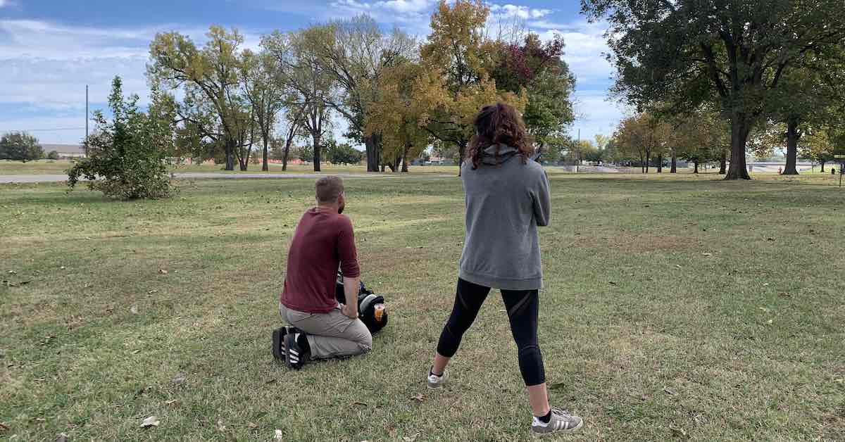 Kneeling man and standing woman on disc golf course as seen from behind