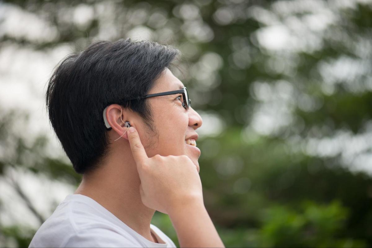 online hearing aids: person pointing at his hearing aid while outdoors