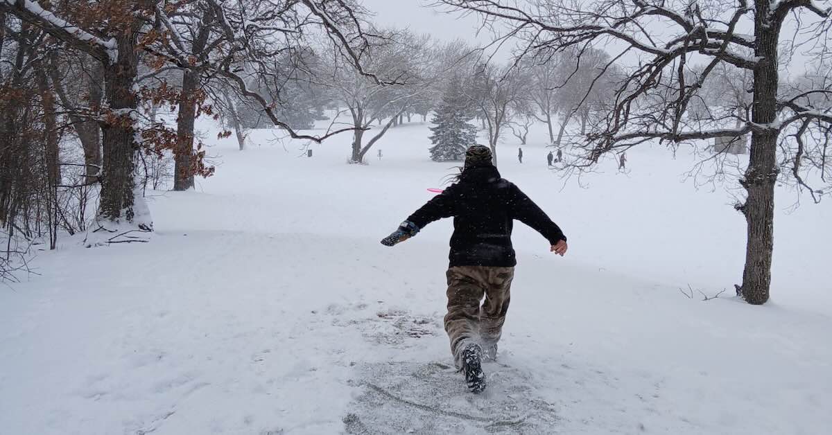 A man in a very snowy area after releasing a disc golf drive