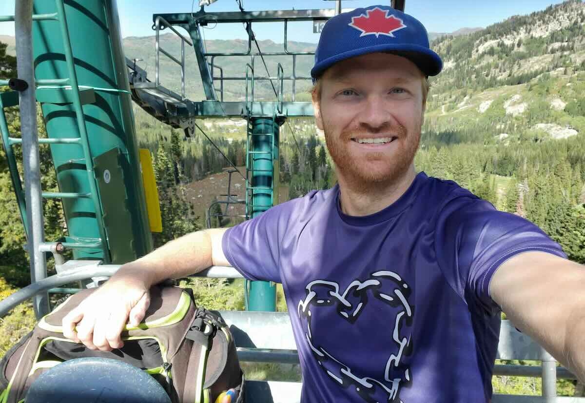 A man in a selfie on a ski lift with a disc golf bag