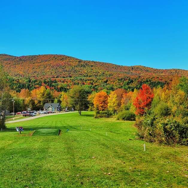 A mown area with a hillside covered in trees in fall colors