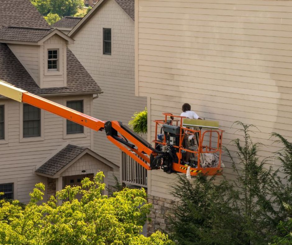 Boom lift with a man in it painting the side of a house