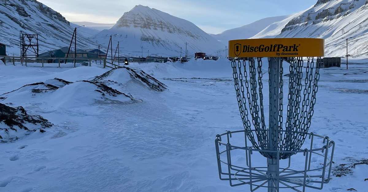 A yellow-banded disc golf basket in a snow-covered, mountian landscape