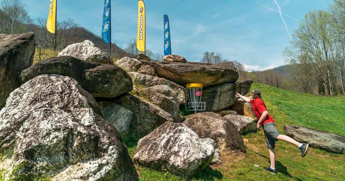 A man putts into a disc golf basket tucked among large boulders