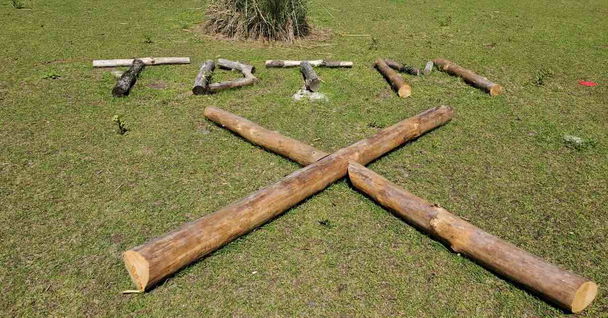 Logs arranged on grass to make the letters TDTM and a large X