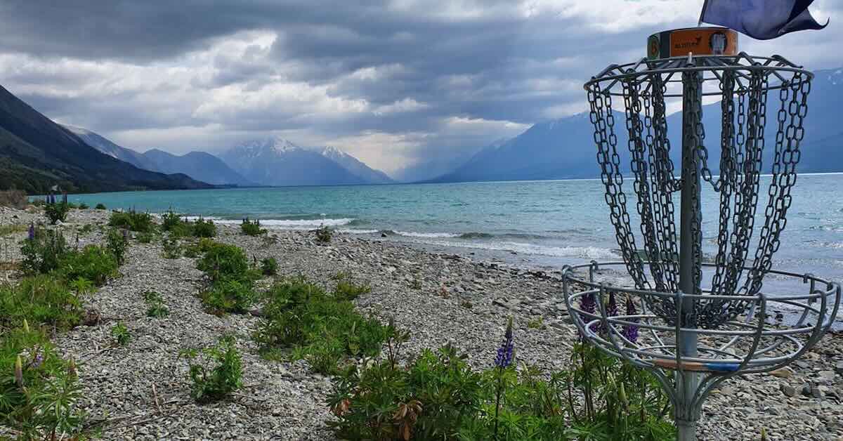 A disc golf basket in front of a dramatic backdrop of water and mountains