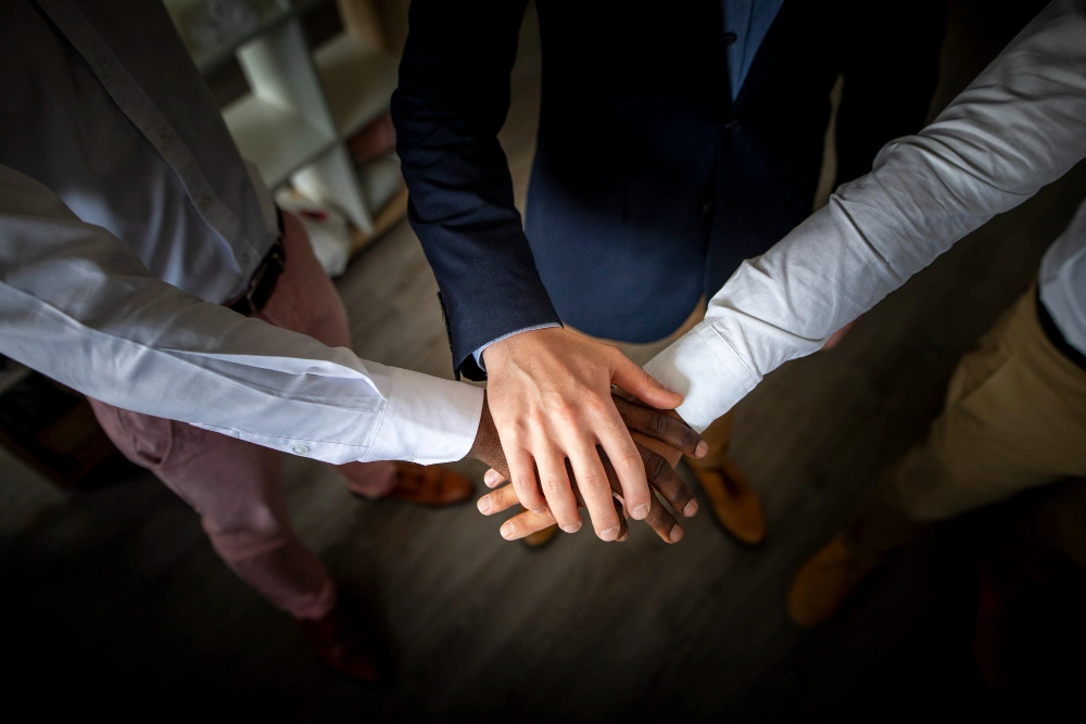 Close-up of multiple hands of diverse individuals coming together in a group huddle, symbolizing teamwork and unity.
