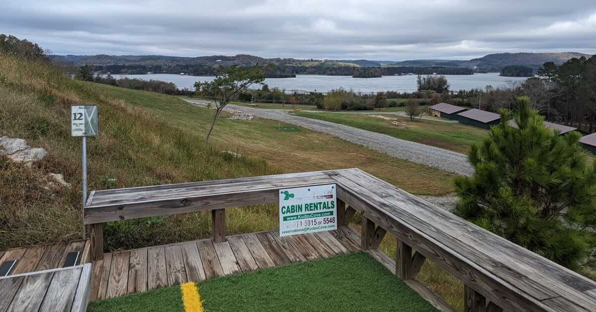 A disc golf tee pad on a wooden platform with a view of hills and a lake beyond