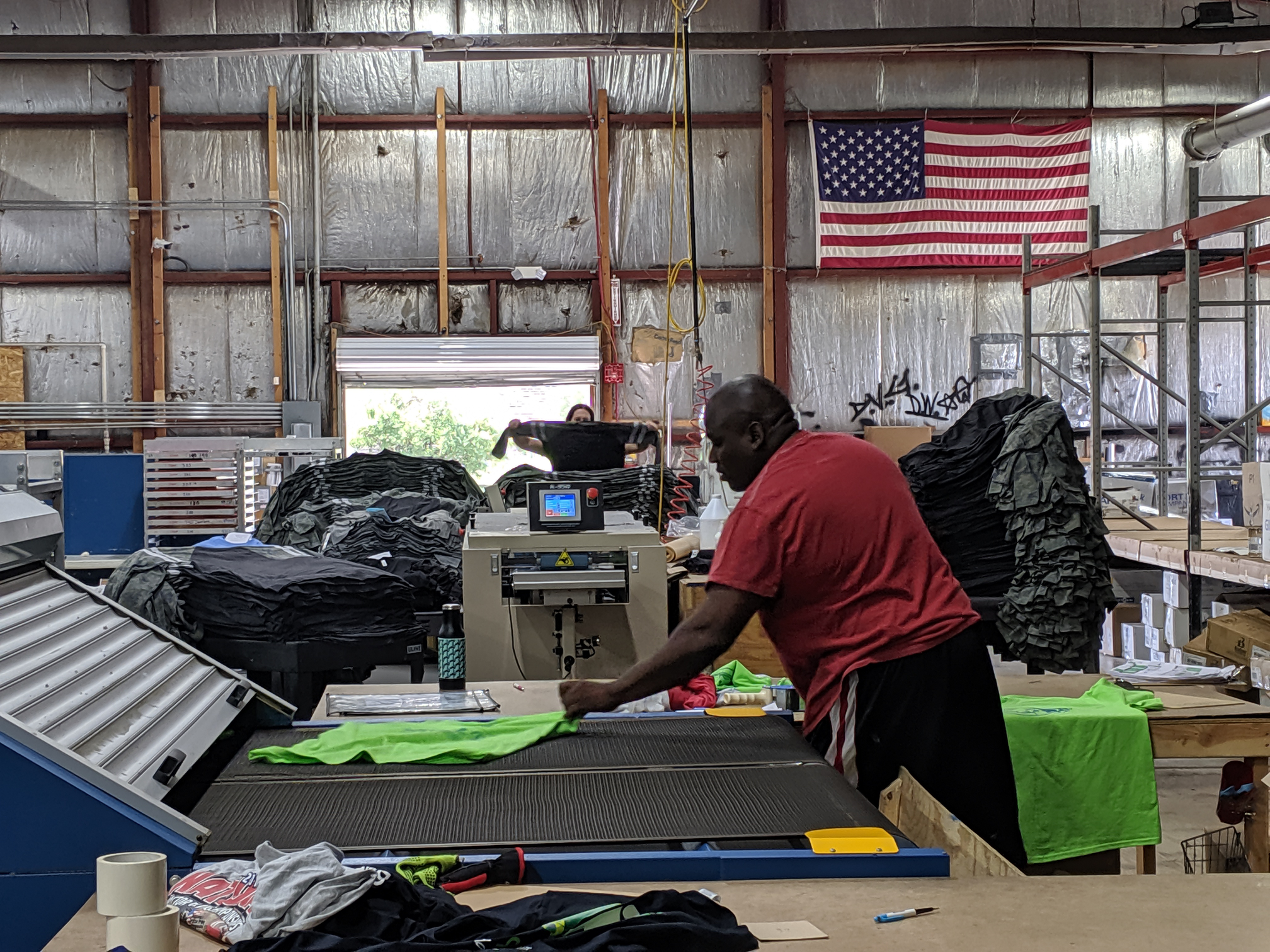 A screen printer helps grab shirts off a conveyor dryer.