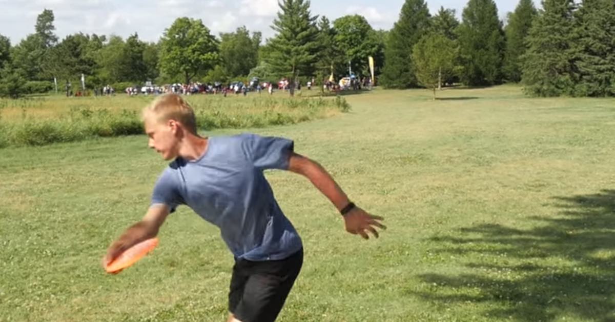 Young man with a blue shirt reach back during a disc golf throw in an open area