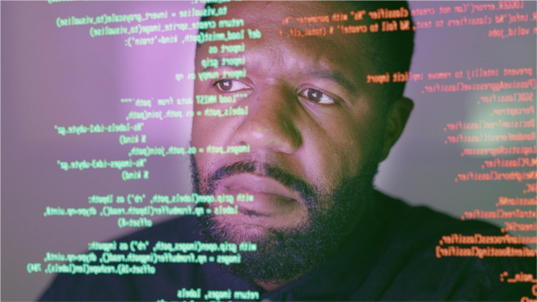 close up of a man’s face looking through a clear screen displaying python script