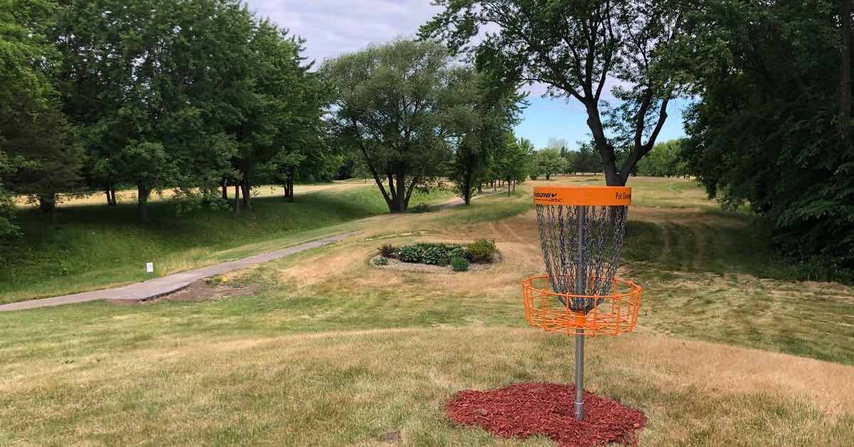 An orange disc golf basket in a mowed area with scattered mature trees