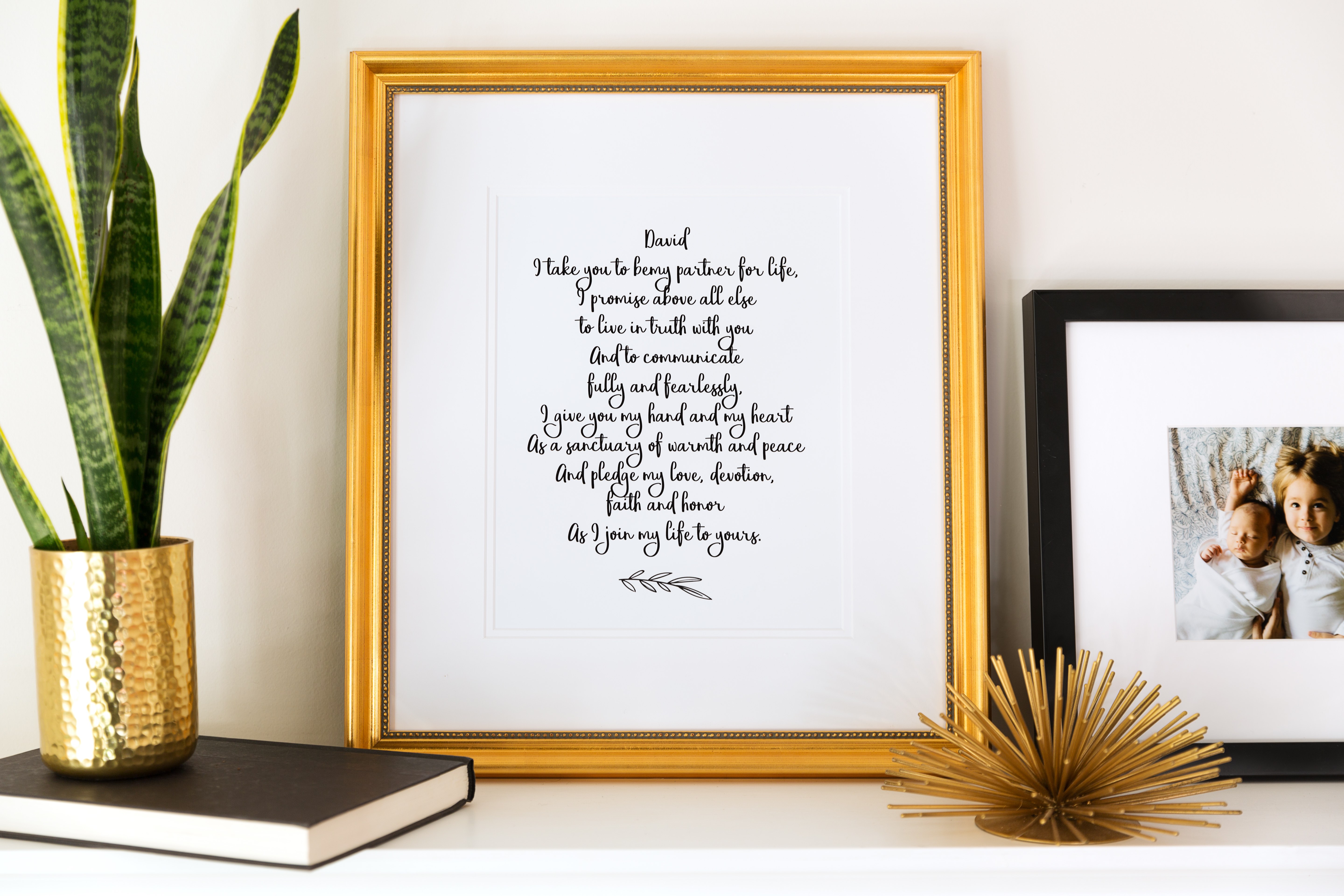 black calligraphy wedding vows in gold beaded frame on white mantle 