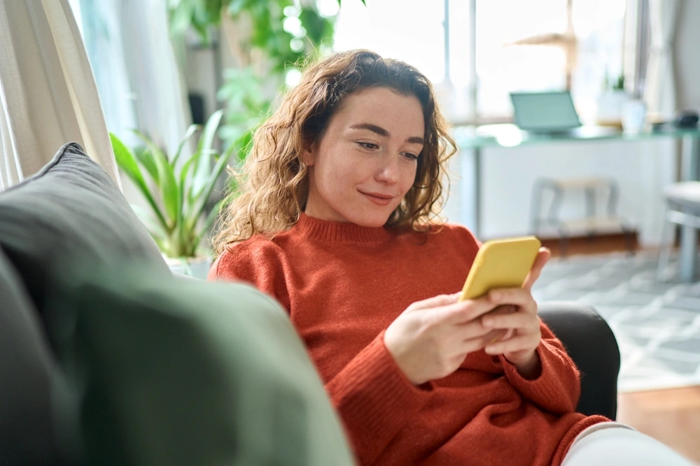 Happy young woman in red jumper using yellow phone
