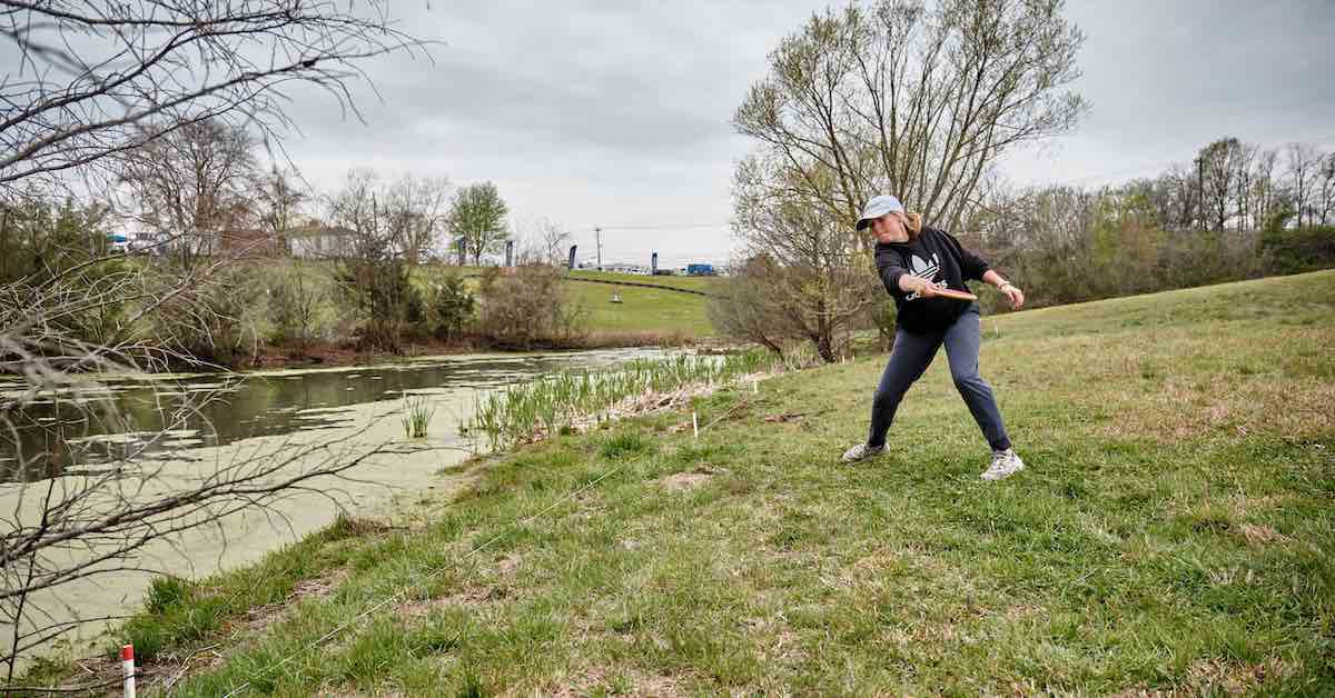 Woman reaching back to throw a disc golf disc over a body of water