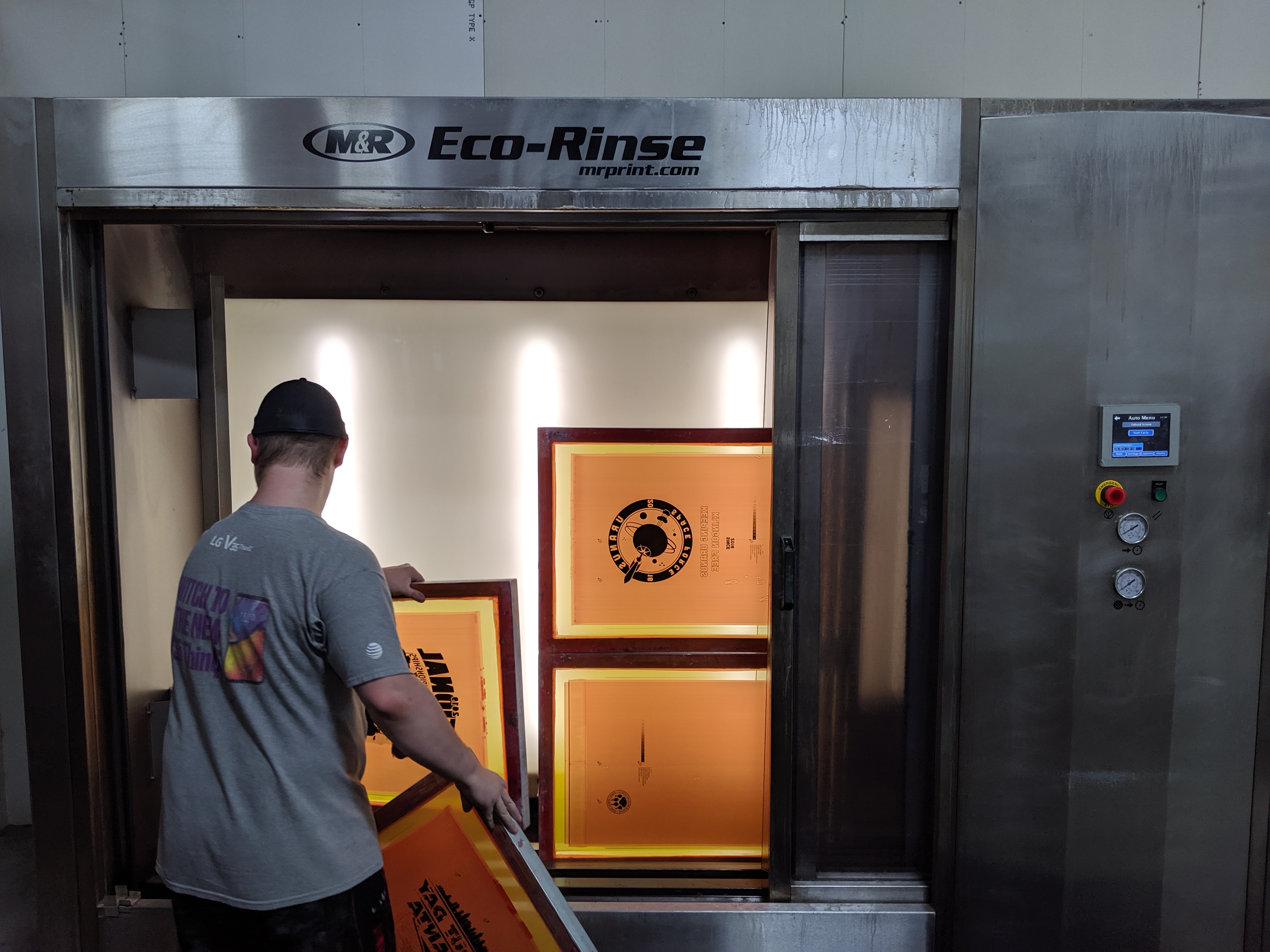 A screen technician washes out screens for screen printing with an automated machine.