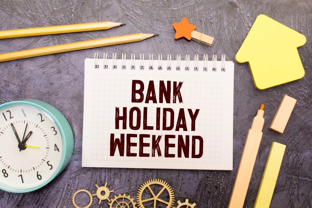 Bank holiday weekend written on paper with sticky notes and pencils next to it.