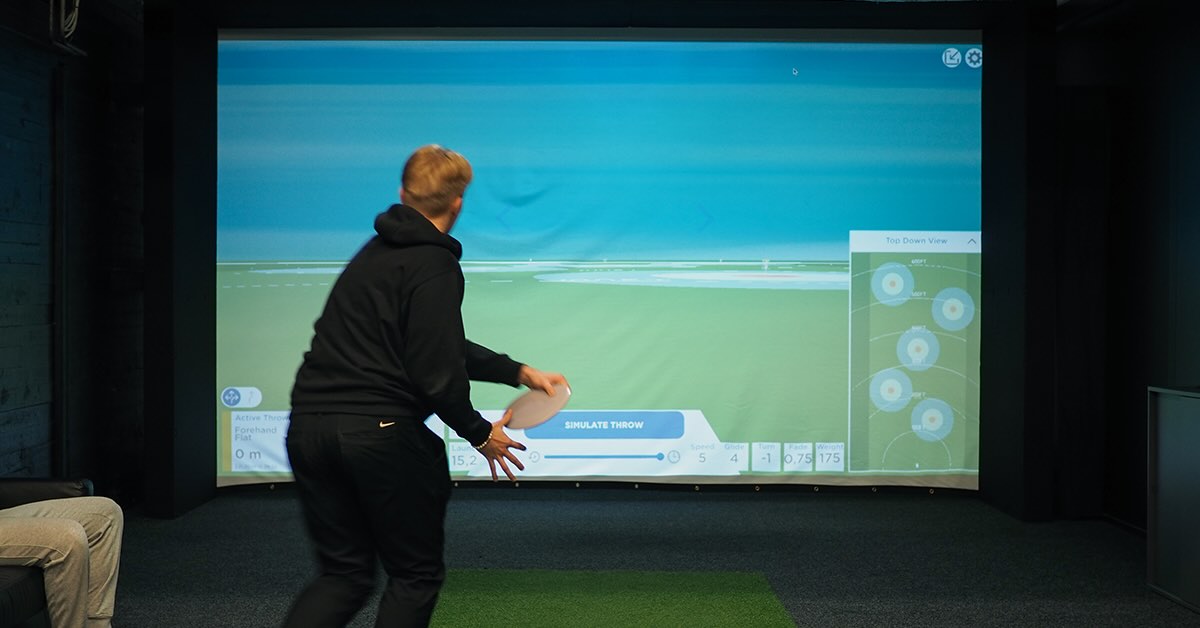 A young man running up to throw a disc golf disc at a projector screen