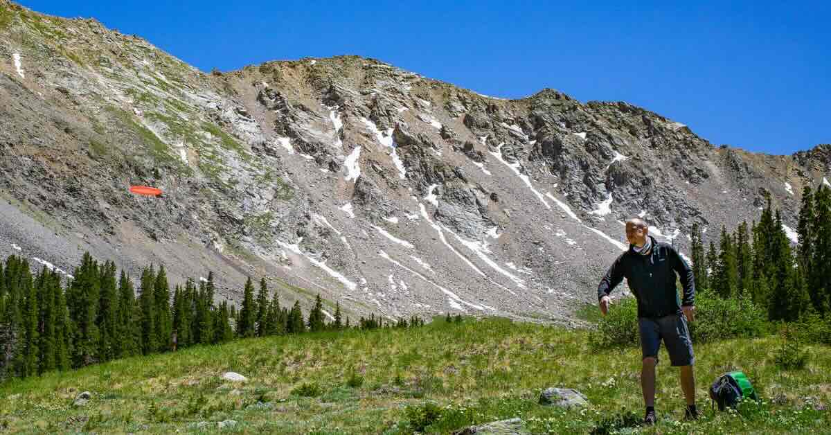 A man putting a disc golf disc with a dramatic backdrop of a rock face in the Rocky Mountains