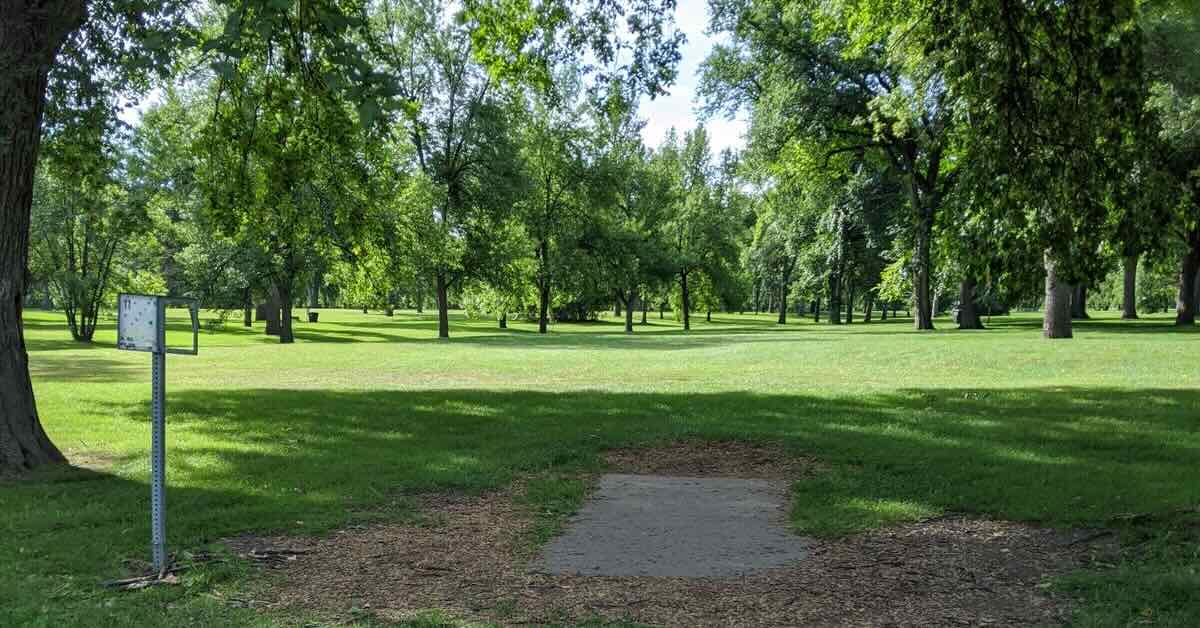 Concrete disc golf tee pad in green grass surrounded by mature trees