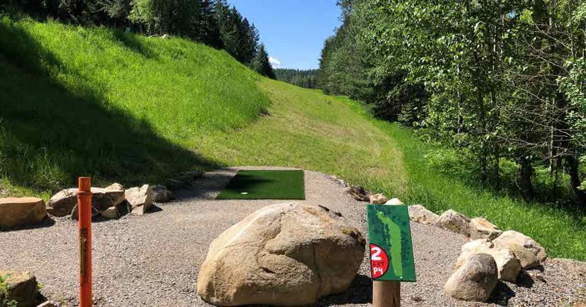 A disc golf tee pad at Caliber Disc Golf Course leads to a well-mown fairway