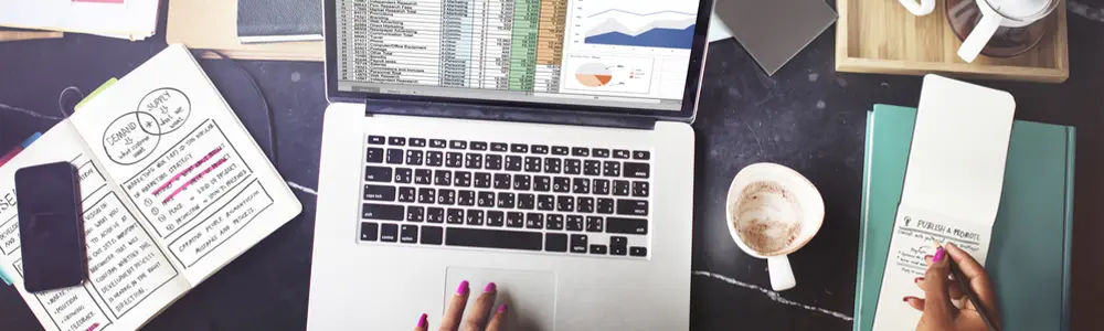 person, laptop and spreadsheets on table