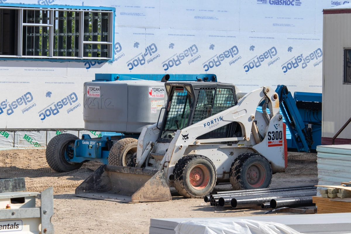 Bobcat skid steer with a bucket attachment and telehandler behind it on a job site