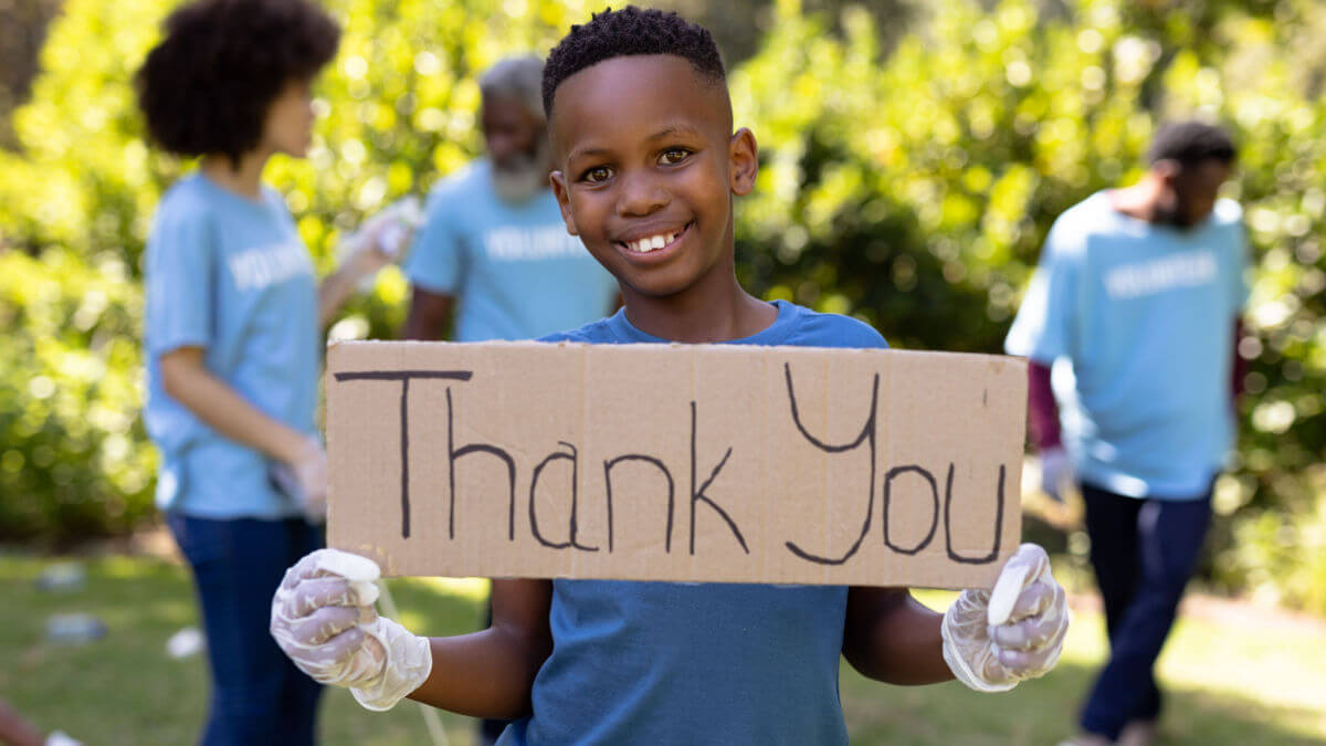 A young black boy shows how to be grateful by holding up a Thank You sign and smiling.