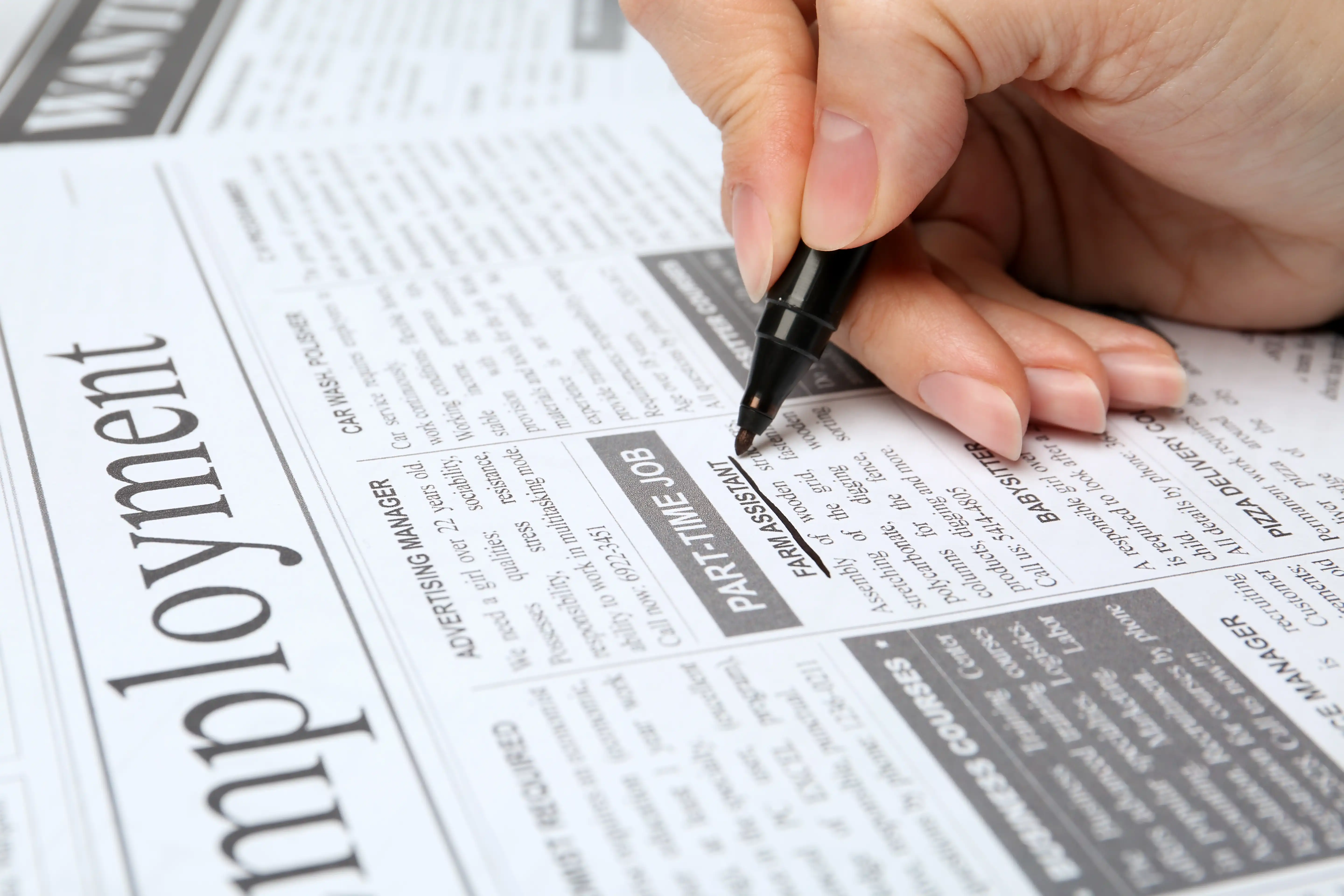 Person highlighting a job listing in a newspaper