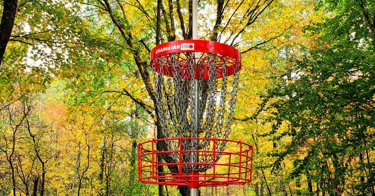 A red disc golf basket with a background of trees in fall yellow
