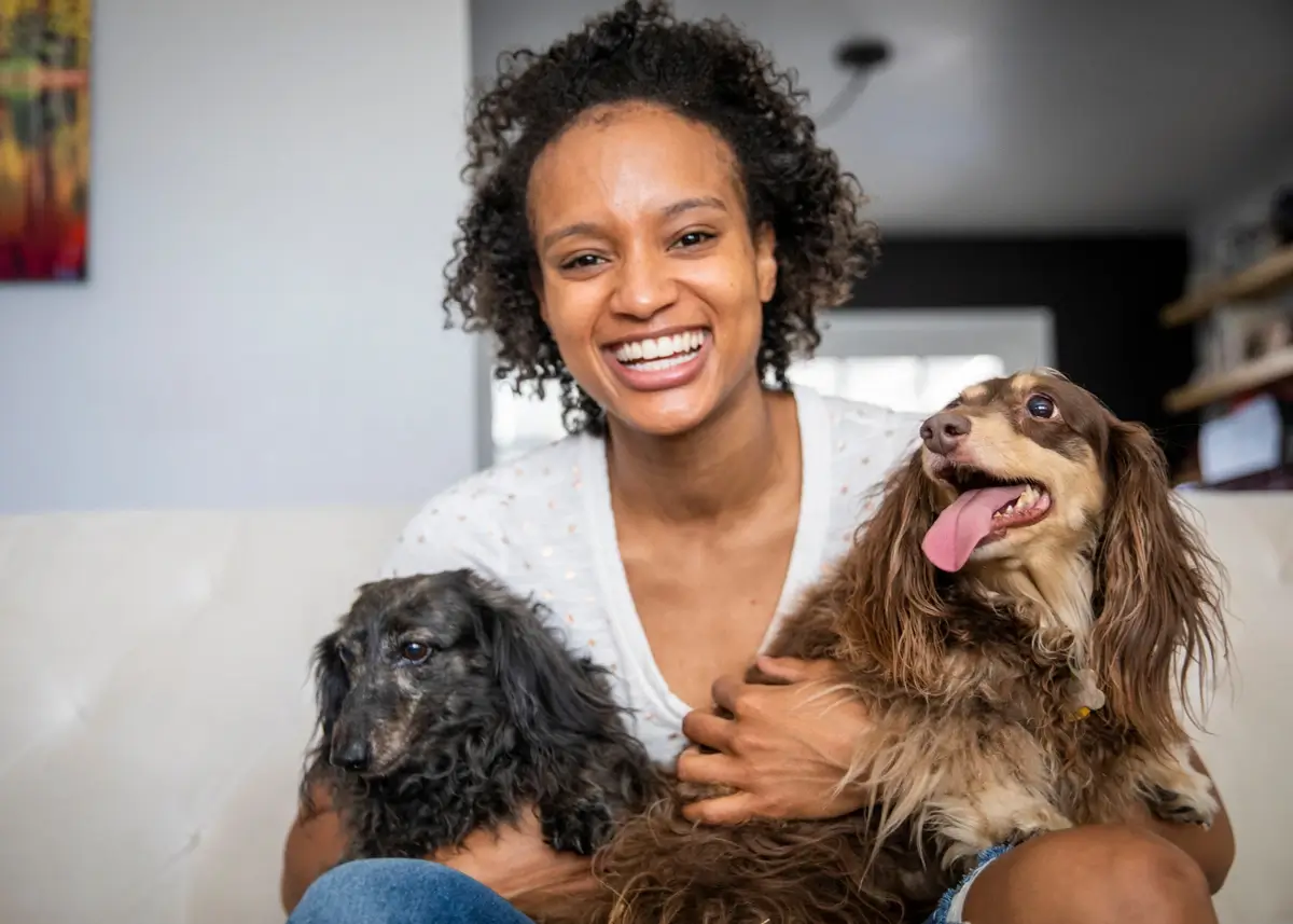 A curly haired woman holds two small shaggy dogs