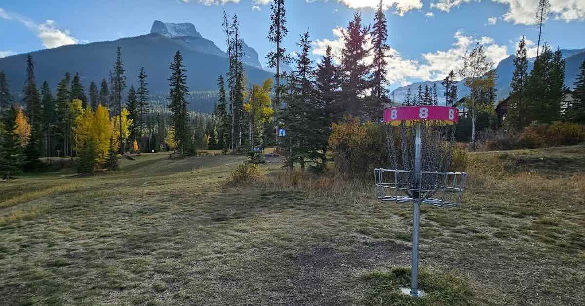 Red-banded disc golf basket with blue sky and mountains in background