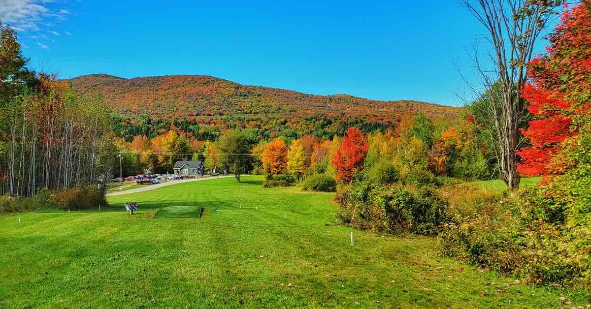 A disc golf tee pad leads to a wooded fairway in fall colors.