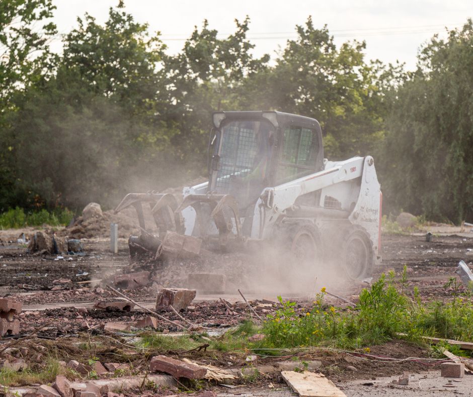 Bobcat skid steer with a grabble bucket attachment on a construction site surrounded by dust