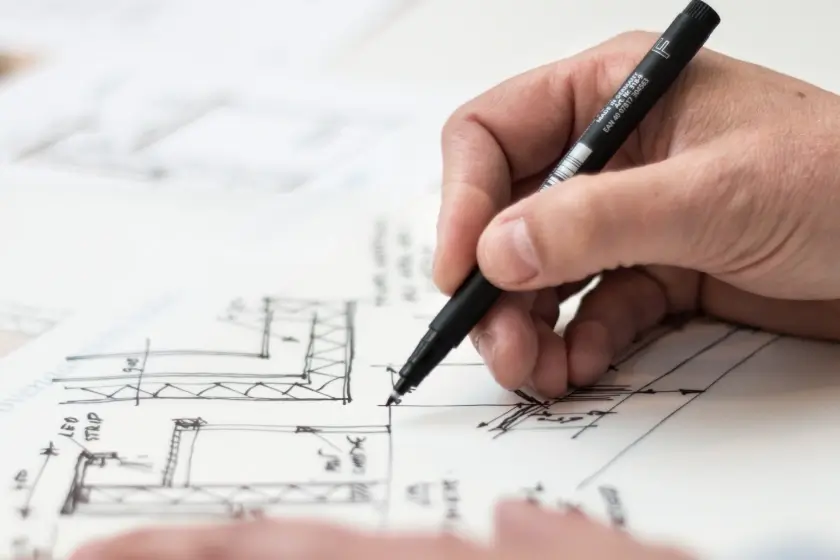 Hands drawing an architectural plan with a black pen