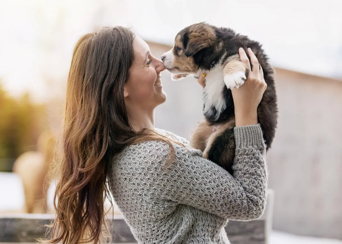 A woman with long hair holds up a Bernese Mountain Dog puppy and nuzzles it
