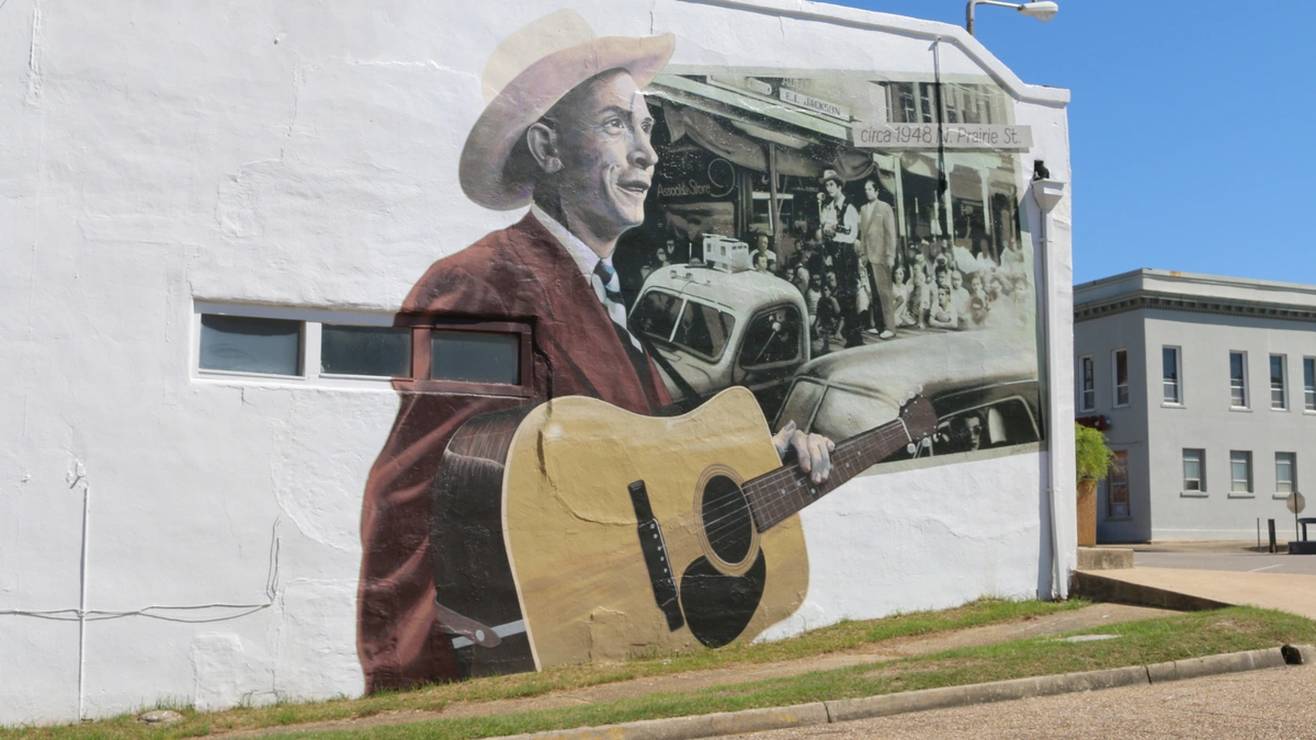 A mural on a building depicting a musician holding a guitar. A small window and a streetlamp are visible on the wall.