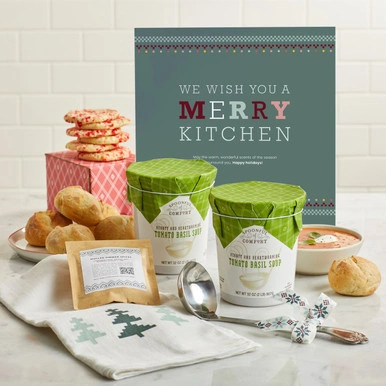 A sign that says "We Wish You a Merry Kitchen" sits next two a couple packages of soup, 6 cookies, a ladel, a kitchen towel, a package of mulled simmer spices and two sets of 3 rolls.