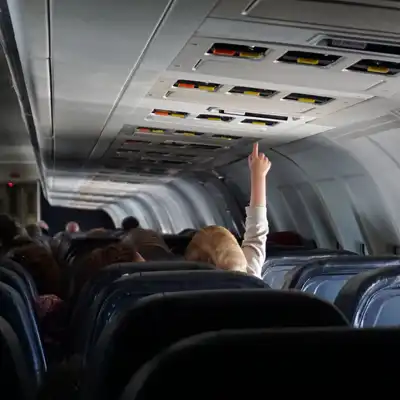 Toddler pushes overhead buttons on an airplane.