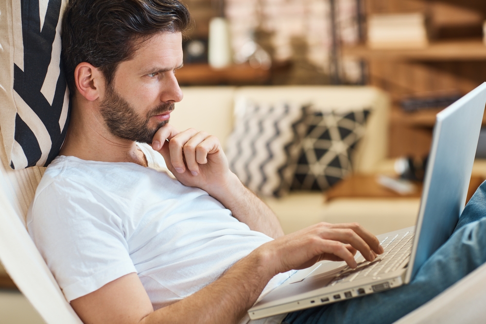 Thoughtful looking white man in t-shirt using laptop