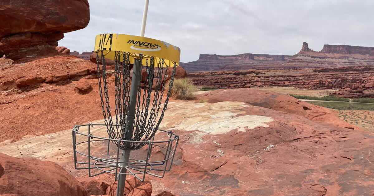 A yellow-banded disc golf basket amid epic red rock desert