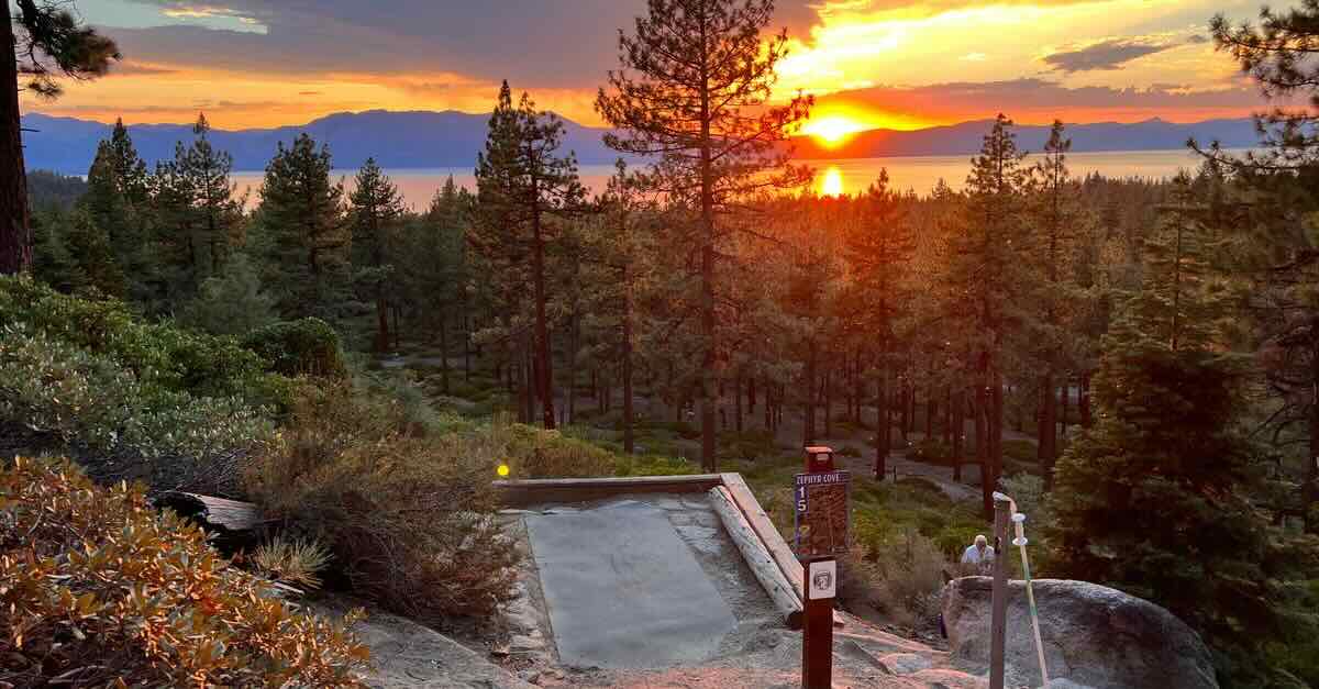 View of a sunset over a lake seen from an elevated position in the scattered trees of a western US forest