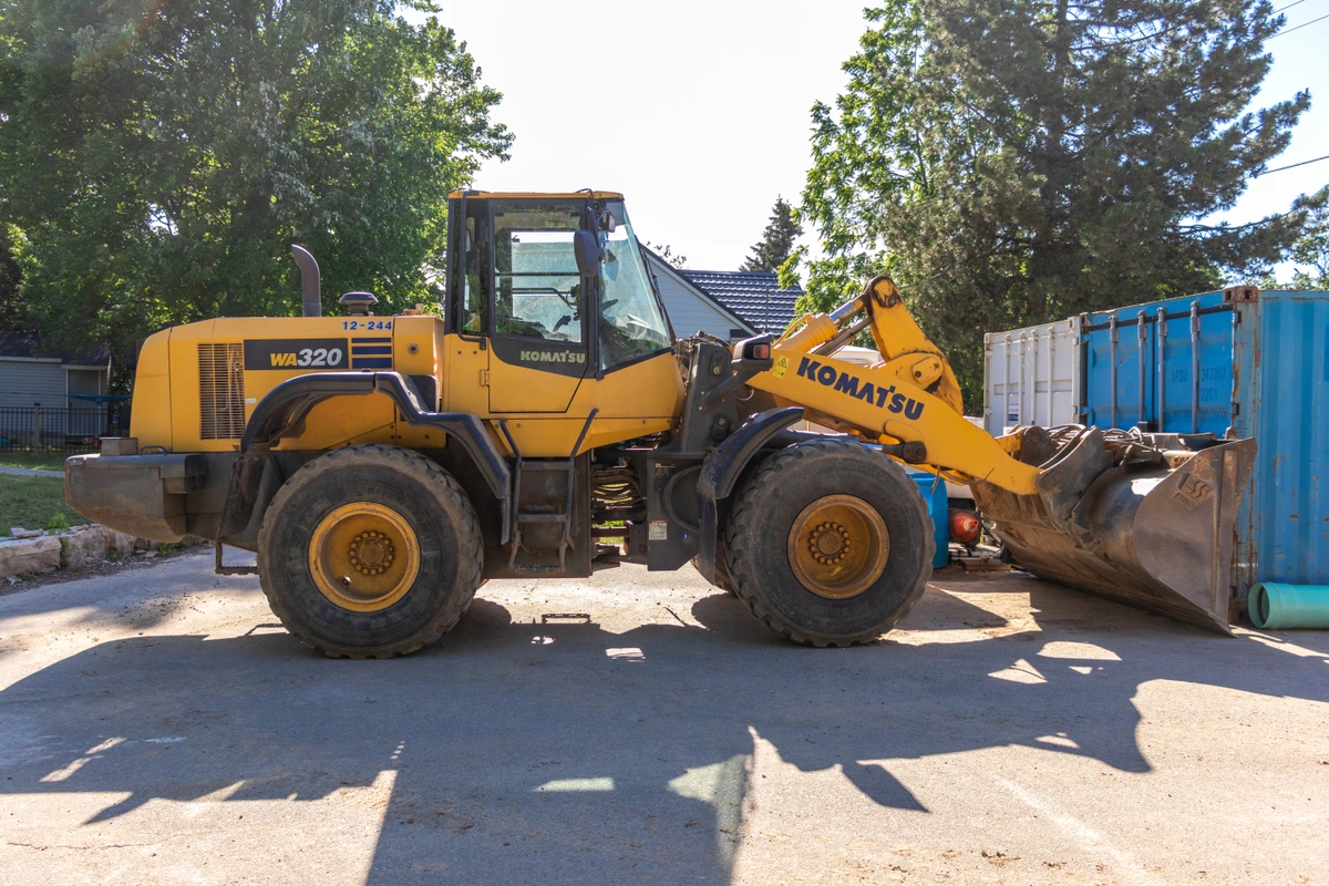 Komatsu WA320 wheel loader with a bucket attachment sitting idle on a site with trees in the background