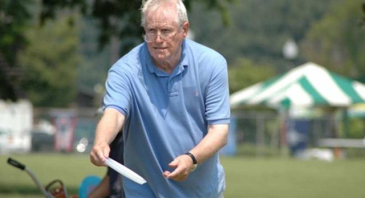 An older man in a blue collared shirt in a putting stance with a disc