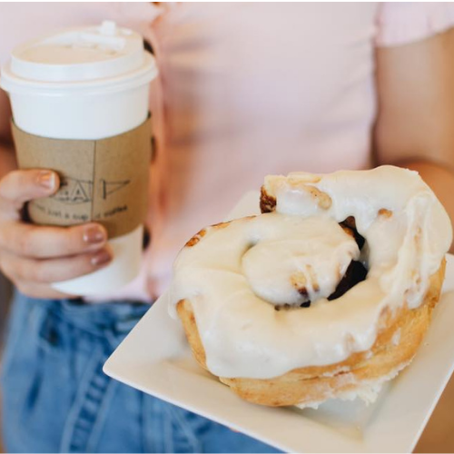 Person holding a coffee cup and a cinnamon roll