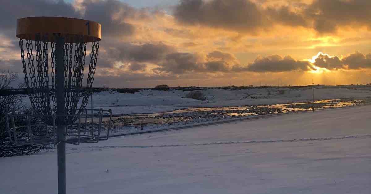 Disc golf basket in snowy landscape with evening light