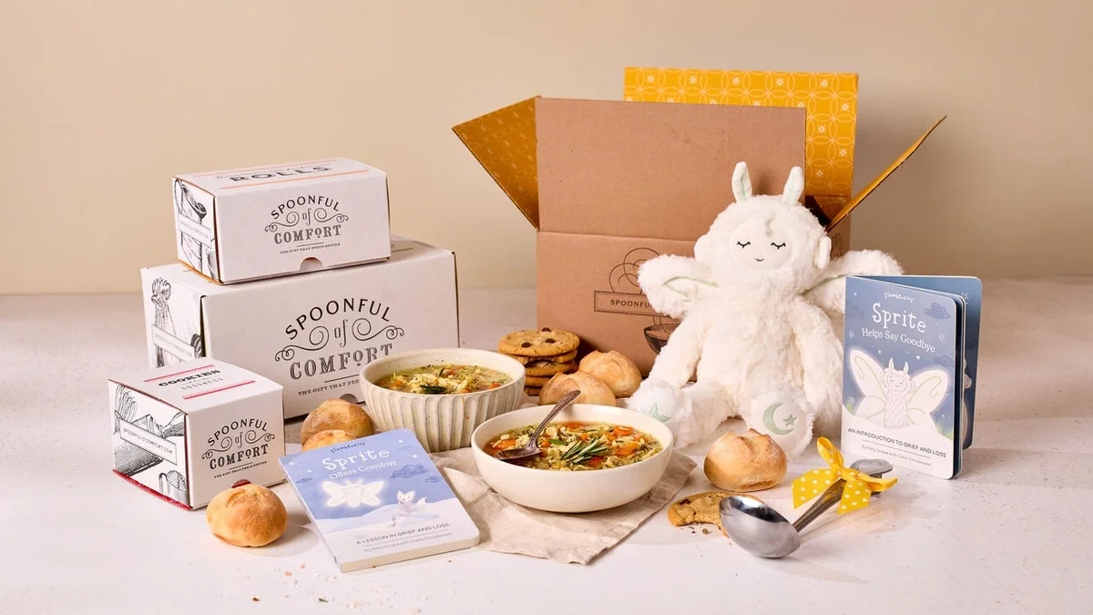 Gift arrangement featuring two bowls of soup, rolls, cookies, a plush Sprite toy, two Sprite children's books, Spoonful of Comfort soup and cookie boxes, and a metal ladle with a yellow ribbon displayed beside an open gift box.