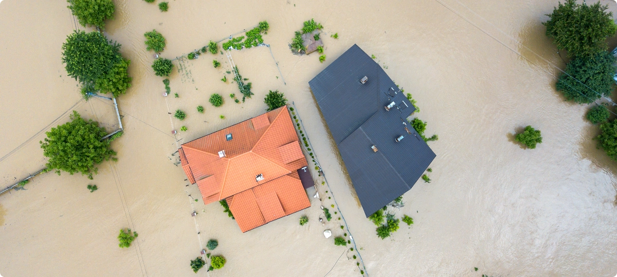 Two houses and the surrounding area seen from above covered with flood waters