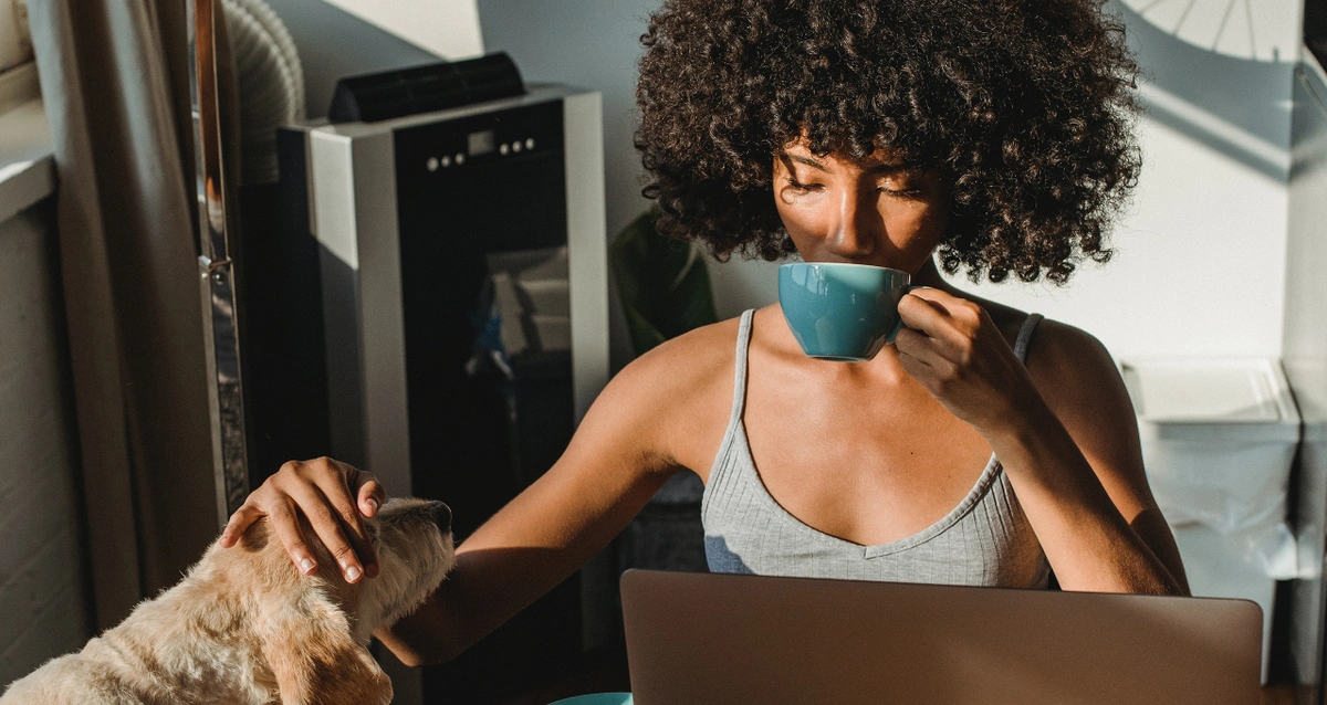 A person petting a dog while searching the internet while calmly sipping from a teacup.